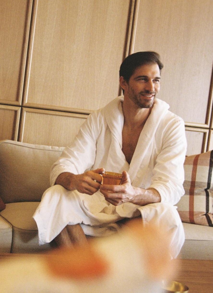 man smiling and relaxing in a spa robe while holding a glass of water man smiling and relaxing in a spa robe while holding a glass of water